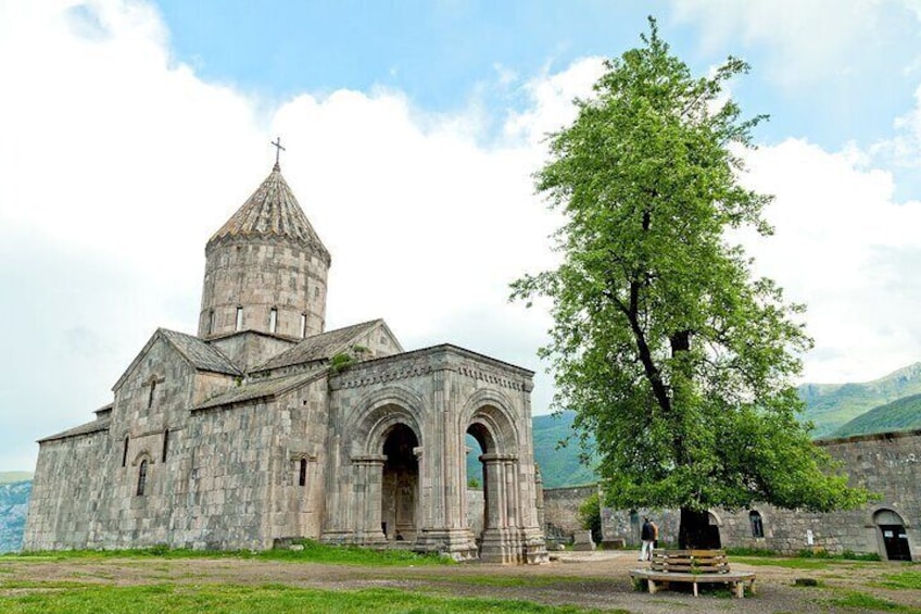Une église en pierre, dotée d’un clocher imposant et d’une entrée en arc de cercle, entourée d’une pelouse et d’un grand arbre. 2