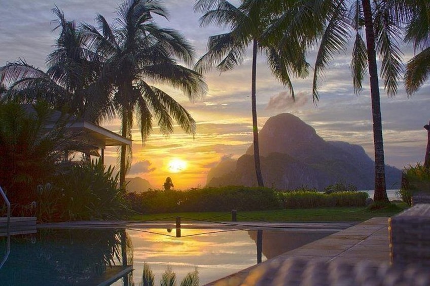 A sunset over a body of water with palm trees and a mountain in the background. 5