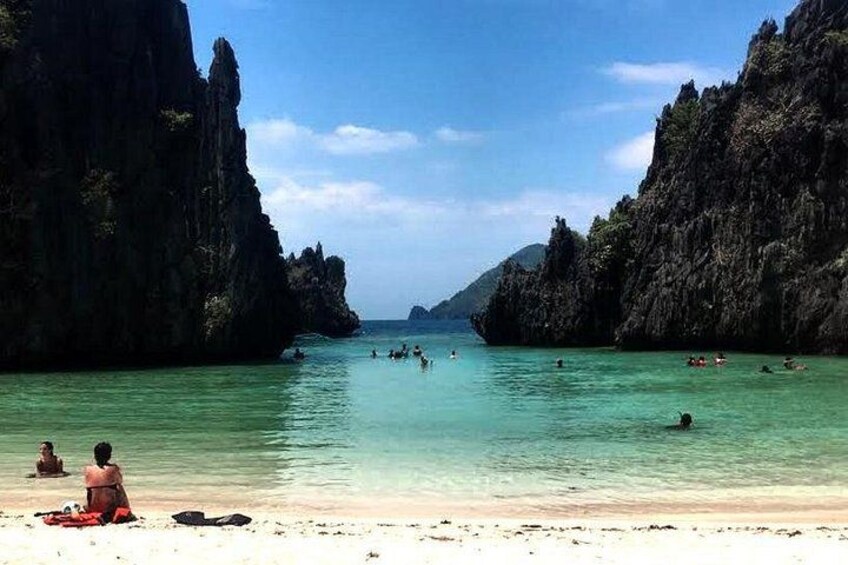 A beach with clear turquoise water, rocky cliffs, and people swimming. 1