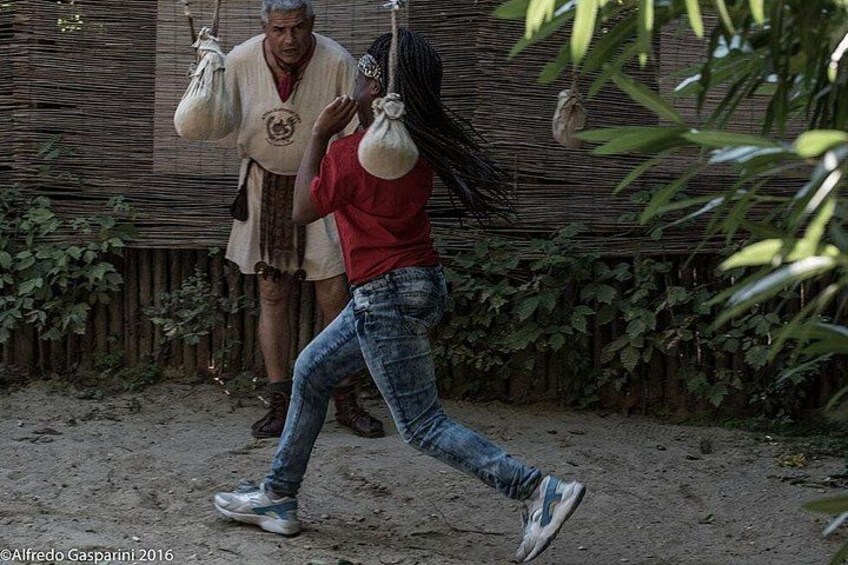 Una persona con camiseta roja y jeans camina sobre un sendero de tierra llevando una cesta en la cabeza, y otra persona con vestimenta tradicional sostiene un saco. 5