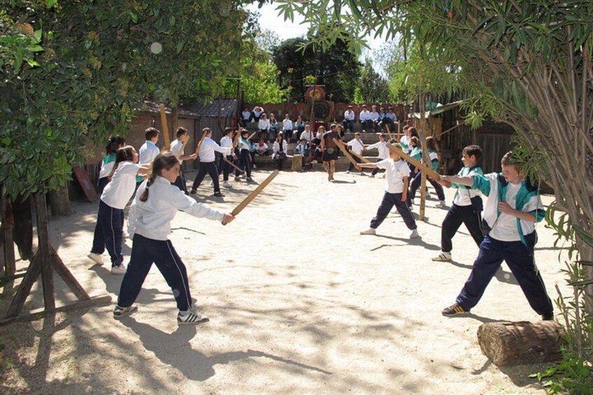 Un grupo de personas practicando artes marciales en un espacio abierto con árboles y suelo de tierra. 2