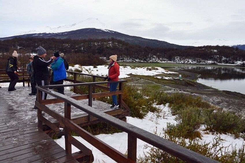 A wooden observation deck with people standing and looking at a lake and mountains in the background. 1