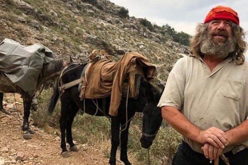 A man standing next to a horse with a saddle and pack. 1