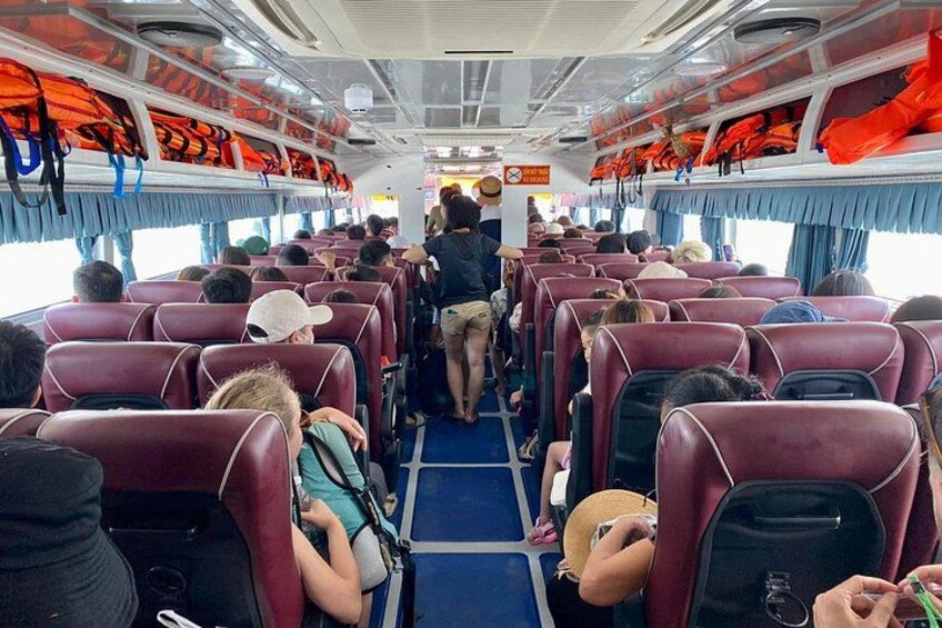 A ferry interior with rows of seats, passengers, and life jackets on the upper deck. 2