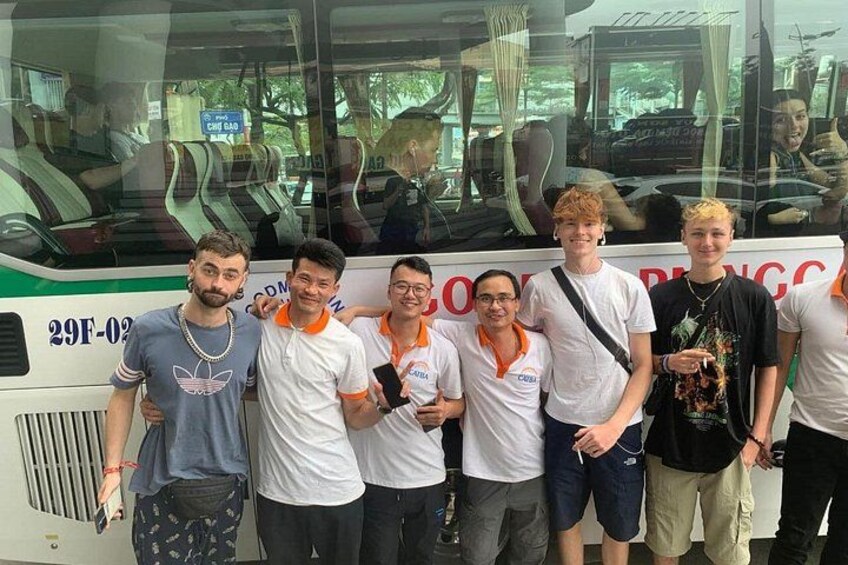 A group of people standing in front of a bus with a reflective window. 1