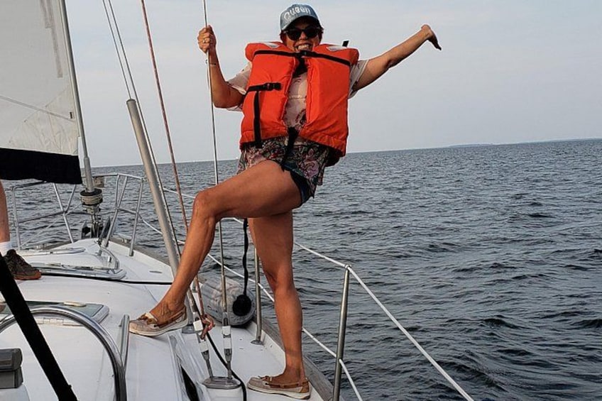 A person on a sailboat wearing a life jacket, holding onto a rope, with the ocean in the background. 5