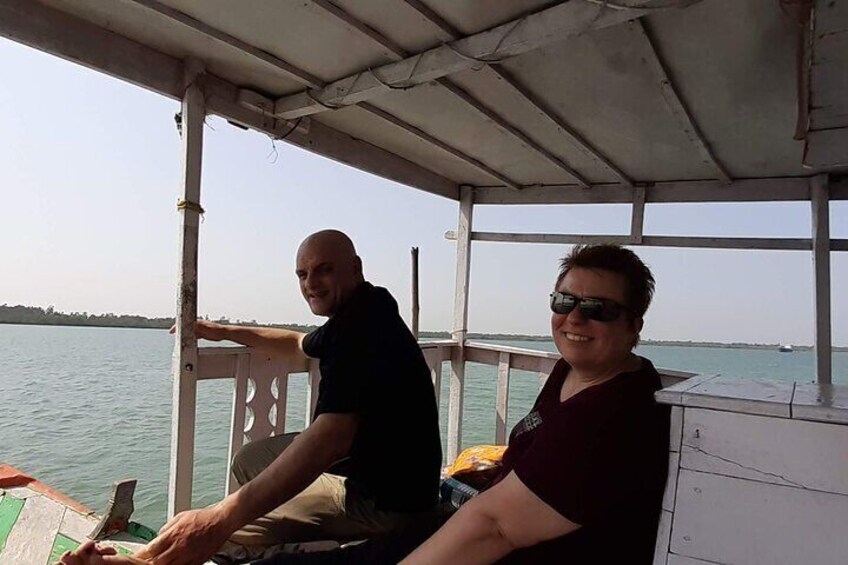 Deux personnes se trouvent sur un bateau muni d’une rambarde, avec de l’eau tout autour et une côte visible au loin. 2