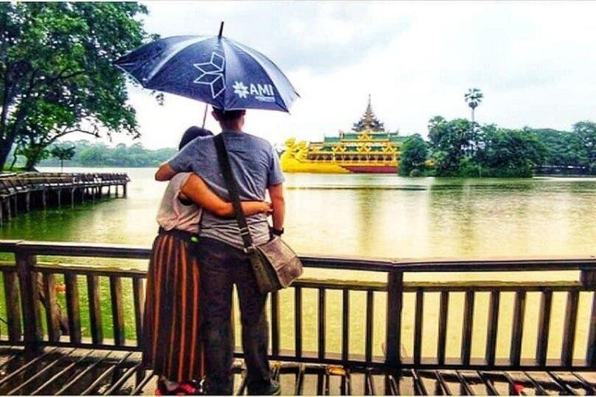 A person holding an umbrella, a yellow boat, and a traditional building by a lake. 5