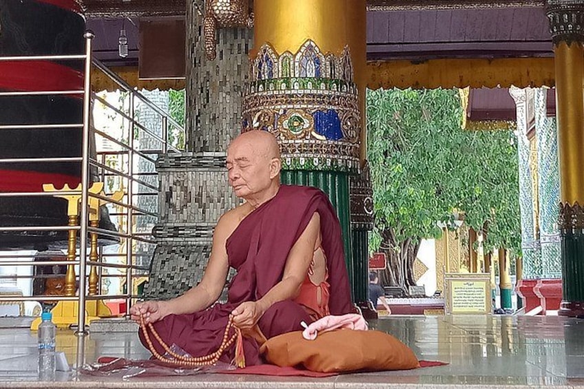 A monk in traditional attire sitting on the floor, holding prayer beads. 3