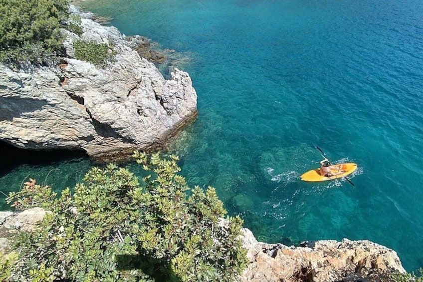 A kayaker on a clear blue sea, surrounded by rocky cliffs and greenery. 5