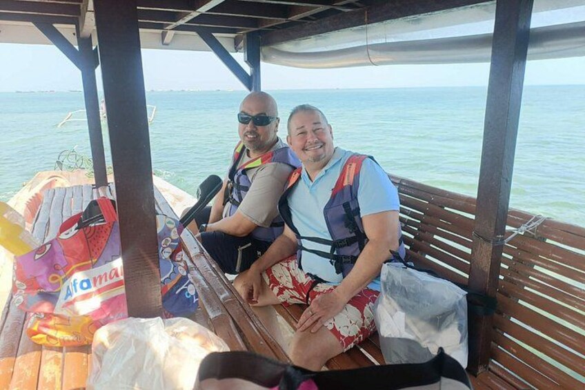Two people on a boat with a canopy, wearing life jackets, and a bag labeled 'Sofitel'. 3
