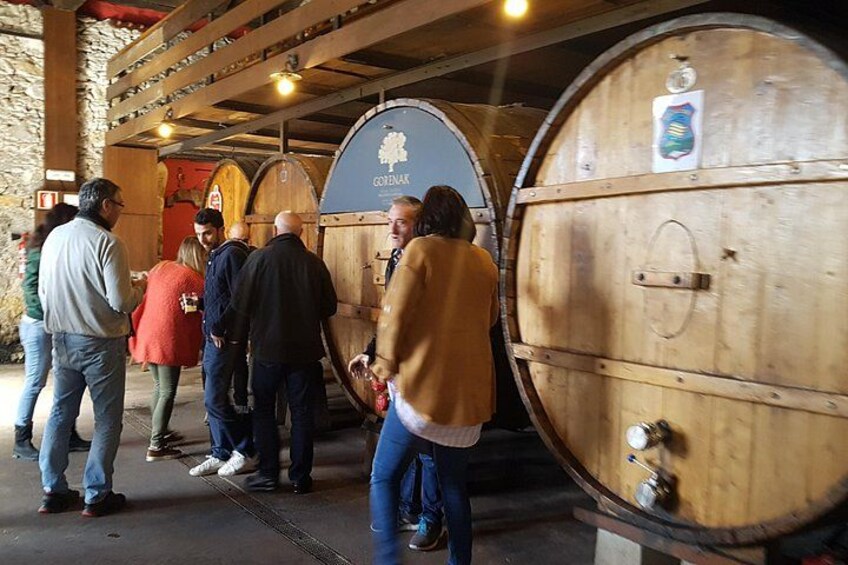 A group of people standing in front of wooden wine barrels in a cellar. 3