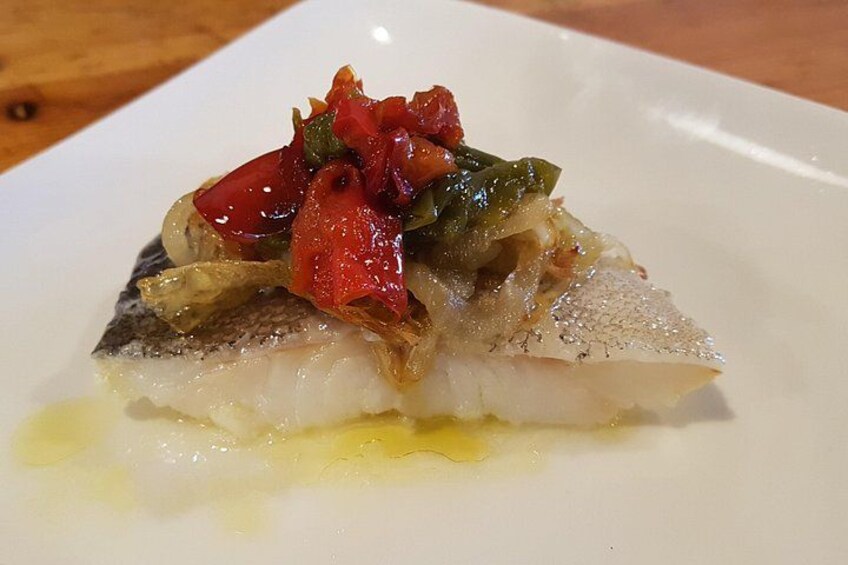A white plate with a piece of fish topped with a red and green salsa. 2