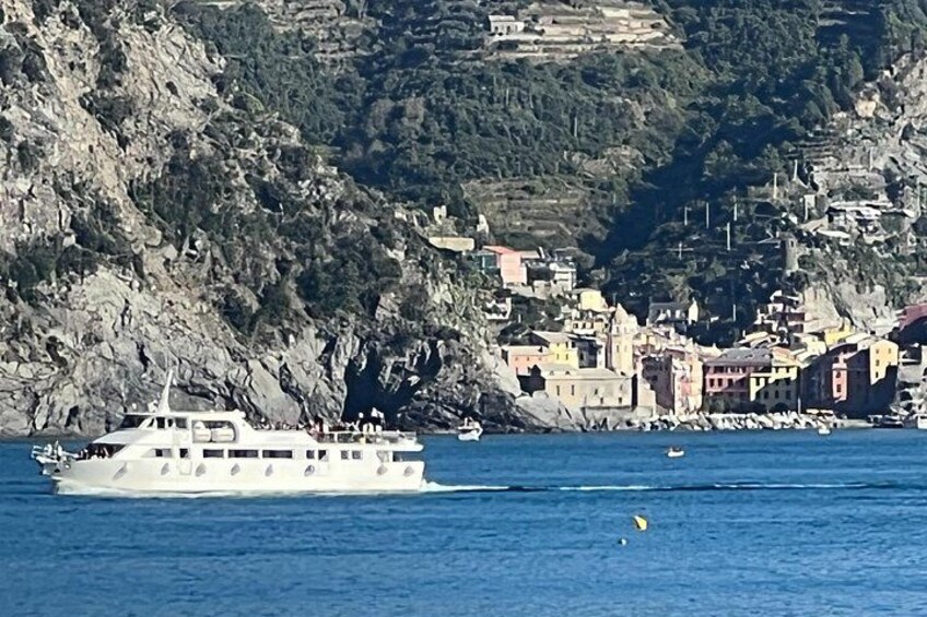 A white boat on calm water, a coastal town with buildings, and a rocky hillside. 3