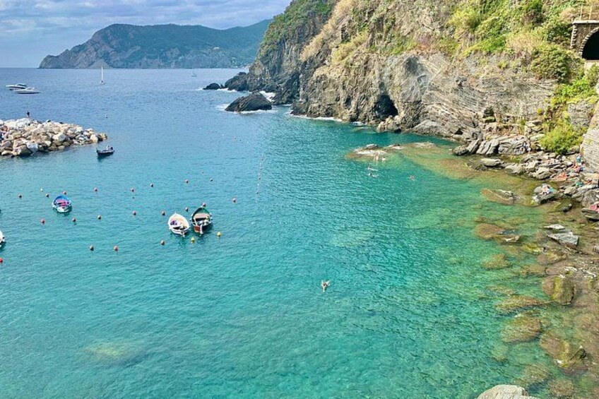 A coastal area with clear turquoise water, rocky shorelines, boats, and a small bridge. 4
