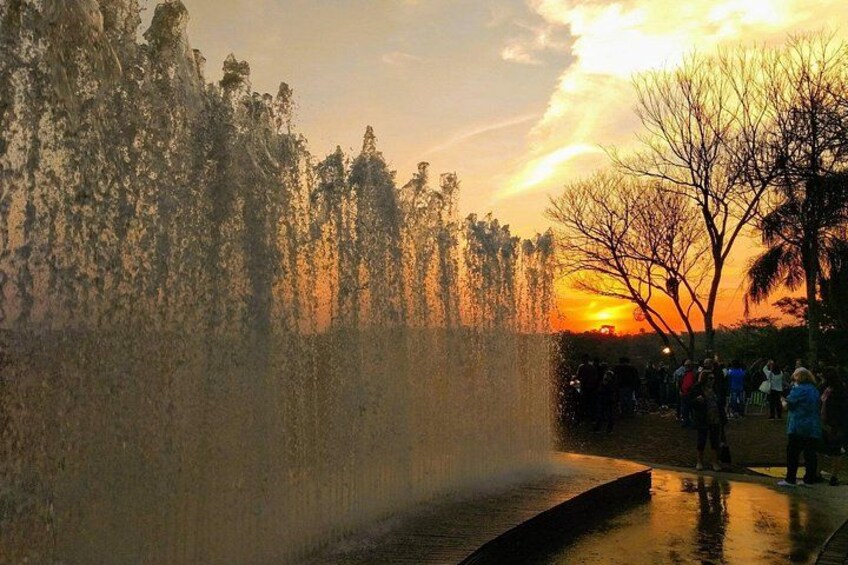 A water feature with a waterfall, trees, and a sunset in the background. 2