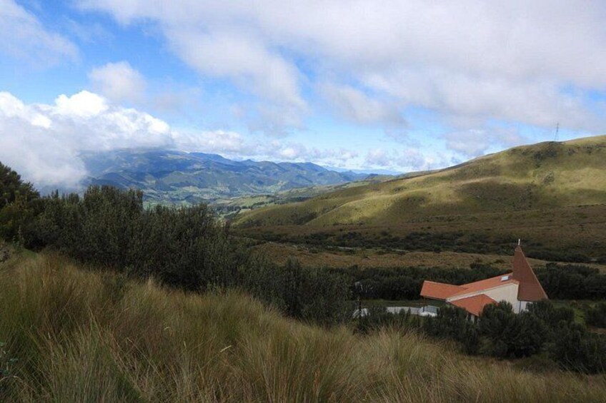 A rural landscape with rolling hills, a red-roofed building, and distant mountains under a partly cloudy sky. 3
