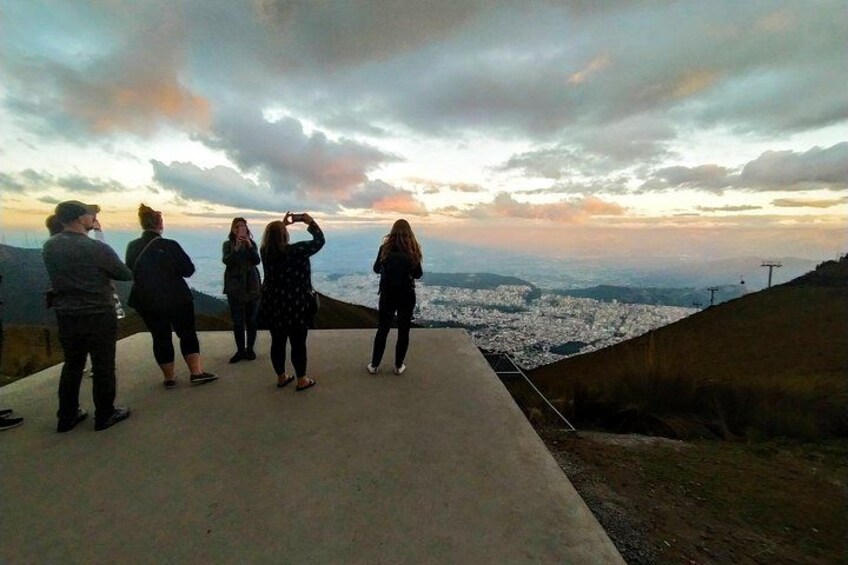 A group of people standing on a concrete ledge overlooking a cityscape during sunset. 1