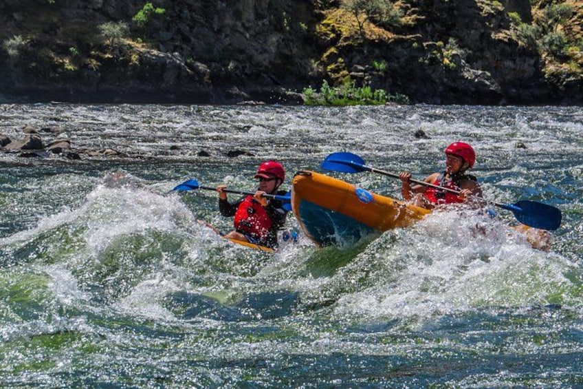 Two people kayaking on a river surrounded by rocky cliffs. 3
