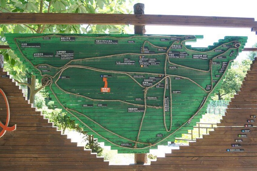 A wooden map with green pathways and labels, surrounded by trees. 4