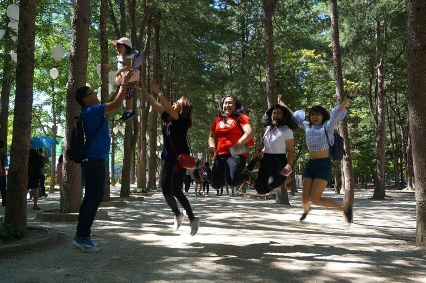 A group of people jumping in a forested area with trees and a dirt path. 5