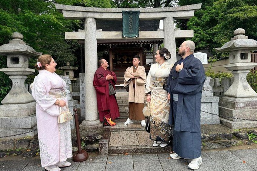 A group of people in traditional attire standing in front of a stone structure with a green sign. 2