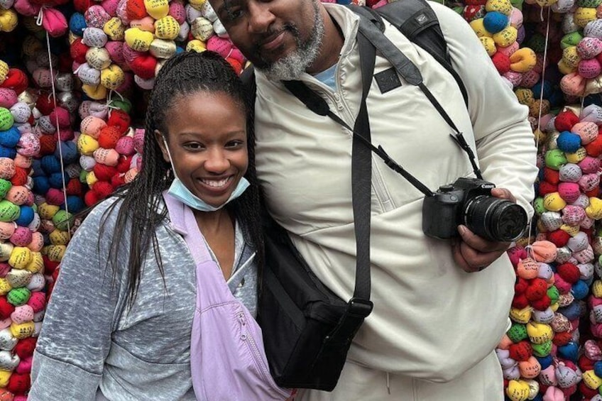 A person holding a camera and standing in front of a wall of colorful balls. 3