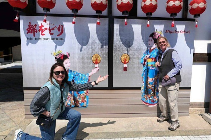 A person in traditional Japanese attire posing with a fan in front of a backdrop with red lanterns and Japanese text. 1
