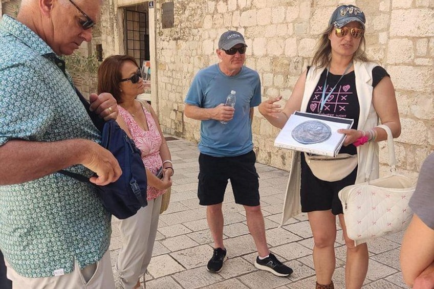 Un grupo de personas de pie al aire libre, algunas sosteniendo objetos, con muros de piedra al fondo. 2