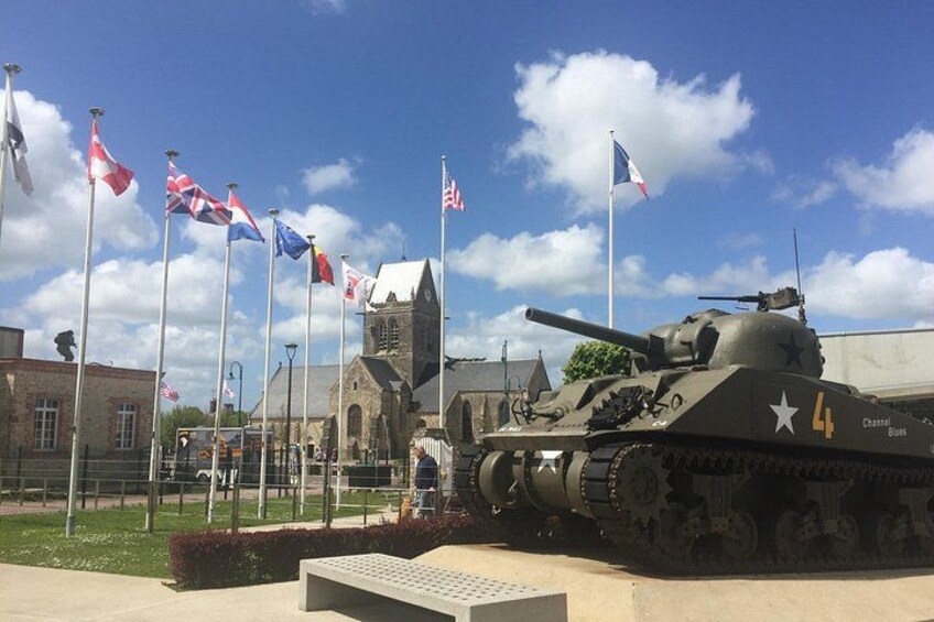 A military tank with the number 4, surrounded by flags, in front of a building with a clock tower. 1