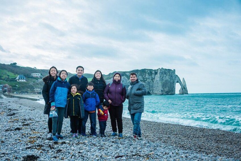 A family on a pebbled beach with a large rock formation in the background. 3