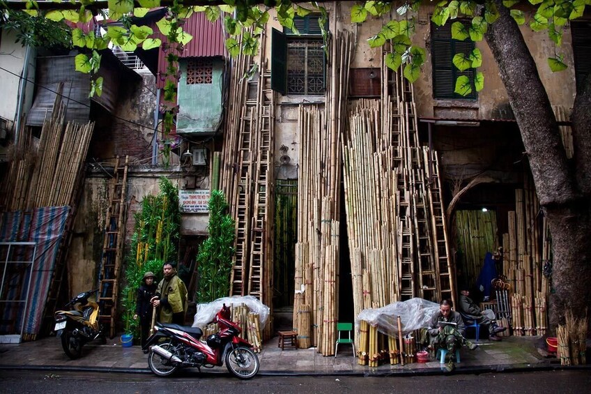 A street scene with bamboo products, motorcycles, and a ladder leaning against a building. 3