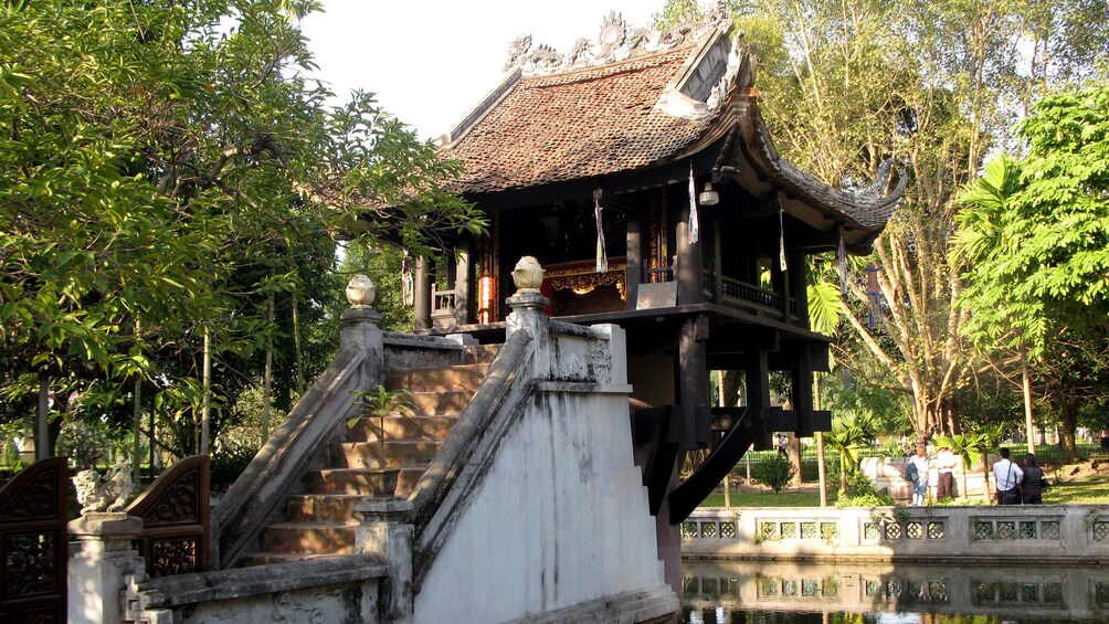 A traditional wooden structure with a tiled roof, surrounded by lush greenery and a calm water body. 1