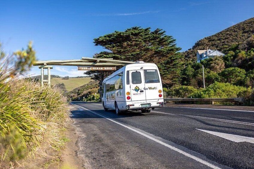 A white bus with 'Go West' on the back driving on a road. 2