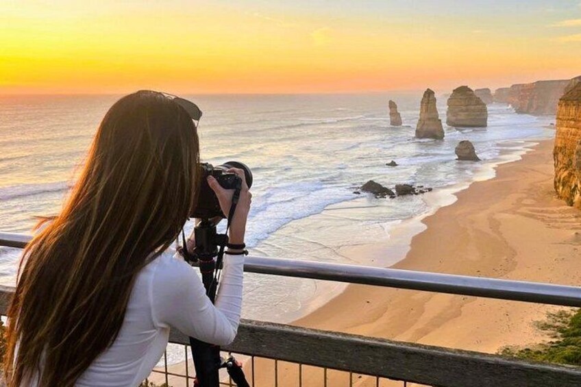 A person taking a photograph of a coastal landscape with distinctive rock formations during sunset. 4