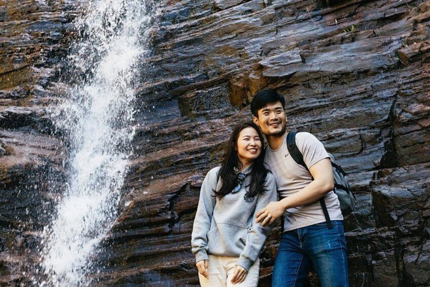 Un couple se tient devant une cascade, avec un paysage rocheux en arrière-plan. 2