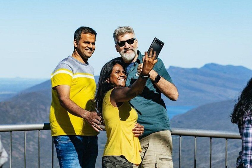 Three people standing on a balcony with a mountainous landscape in the background. 3