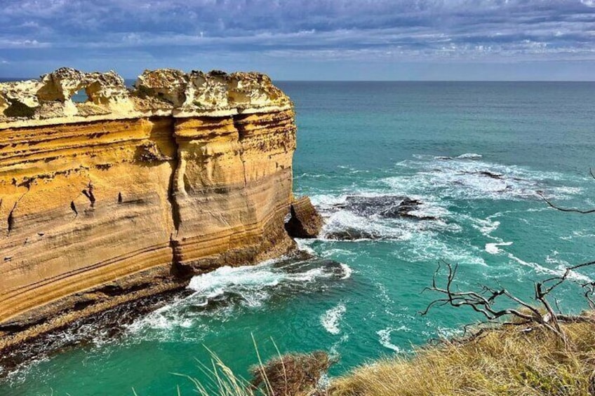 A coastal cliff with layered rock formations and a turbulent sea. 3