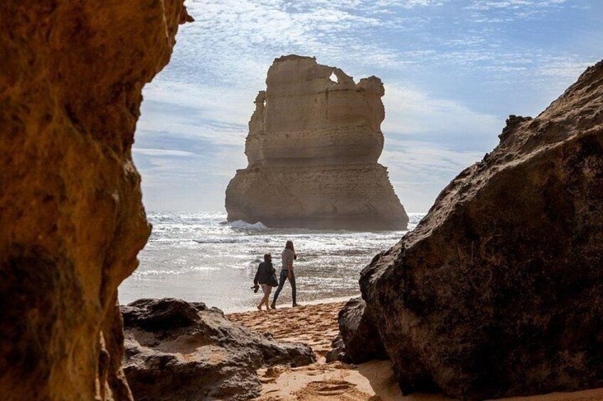 A coastal rock formation with two people walking on the beach. 4