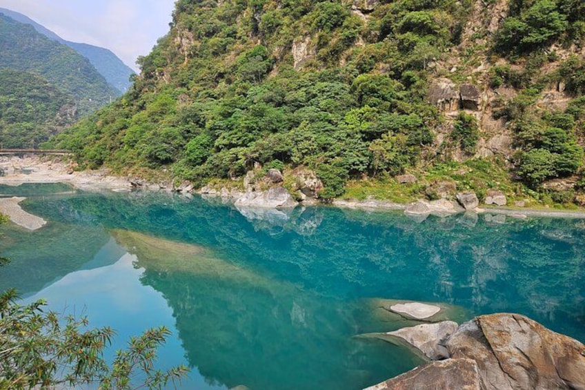 A river with clear water, surrounded by lush green hills and rocky terrain. 2