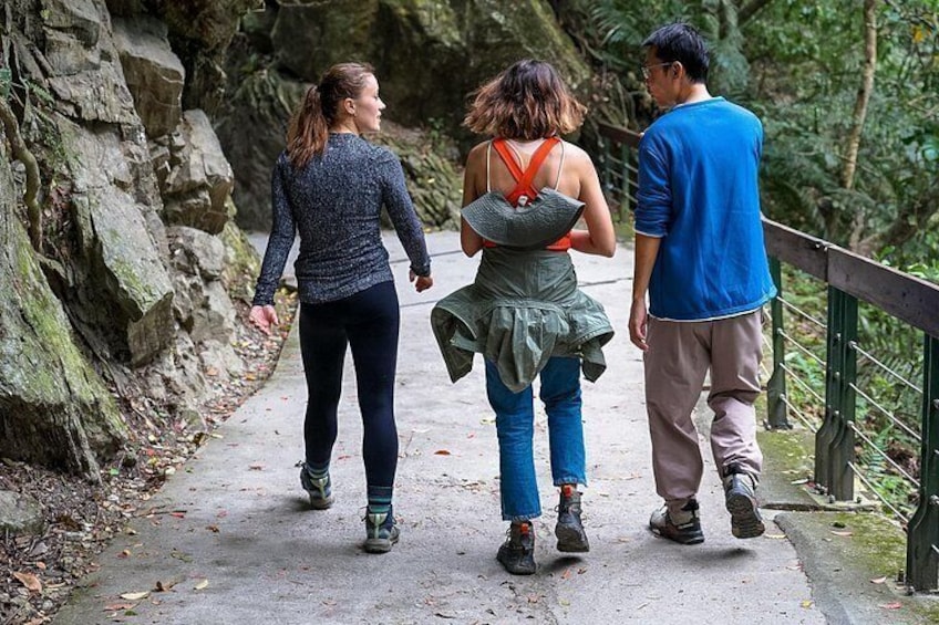 Tre personer promenerar på en gångstig av betong, omgiven av ett stenigt landskap och grönskande växtlighet. 5