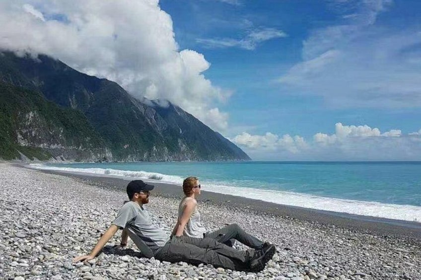 A beach with pebbles, a mountain, and the ocean. 2