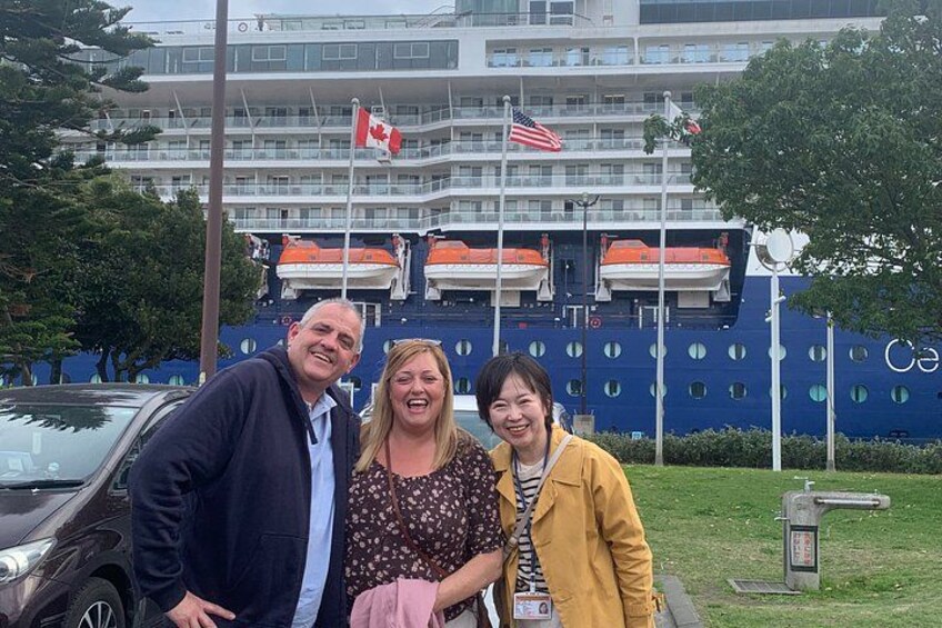 Three people posing in front of a cruise ship with Canadian and American flags. 5