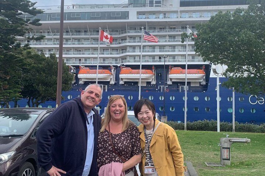Three people posing in front of a cruise ship with Canadian and American flags. 2