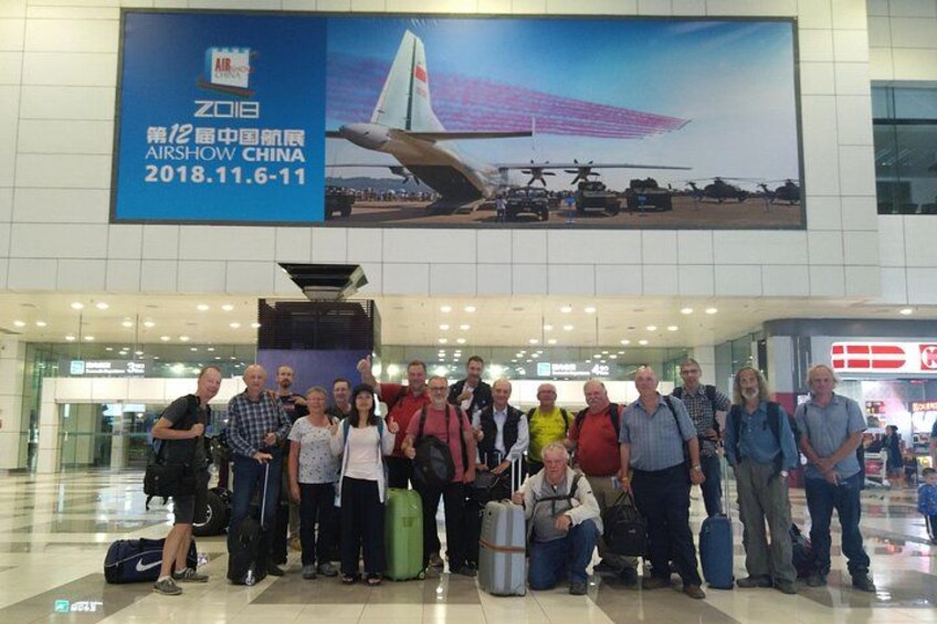 Un groupe de personnes se trouve dans un aéroport, tenant une grande banderole qui fait la publicité d’un salon aéronautique. 3
