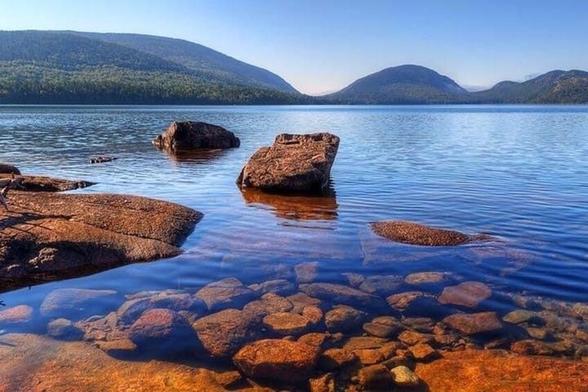 A calm lake with clear water, rocks, and mountains in the background. 2