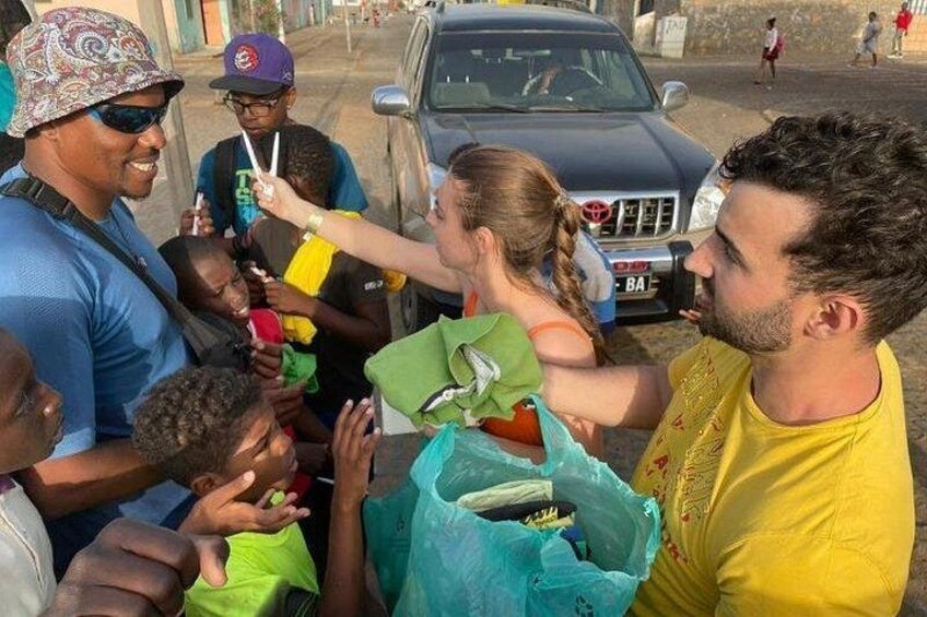 A group of people outdoors, some holding items, with a vehicle in the background. 2
