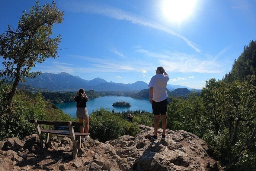 Two people standing on a rocky outcrop overlooking a lake with mountains in the background. 4