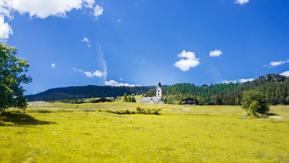 A church in a green field with a forest in the background. 2