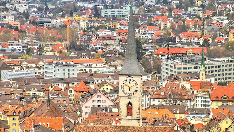 A clock tower with a spire, surrounded by colorful buildings and a dense urban landscape. 5